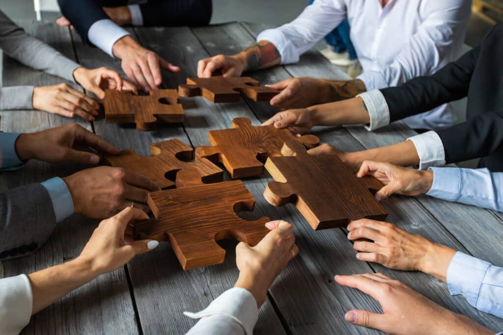 Corporate team building in Calgary: Hands in business attire reaching with large puzzle pieces, symbolizing collaboration and teamwork in a professional setting.